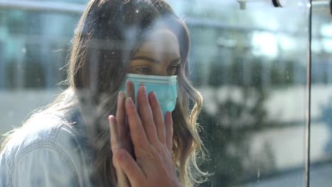 una mujer despejada con máscara está separada o aislada de un ser querido por una ventana de vidrio durante la pandemia del coronavirus