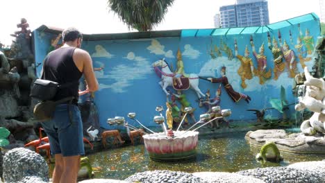 adult male throwing and donating coins at burmese buddhist temple penang