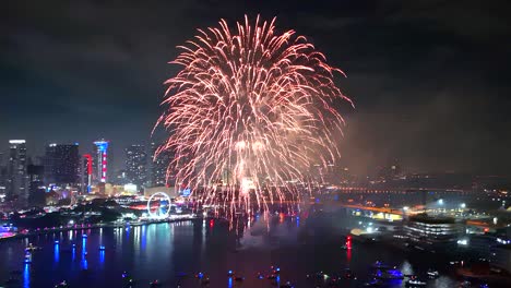 The sky erupts in radiant fire while a drone captures every burst and crackle with glowing boats and towers beneath