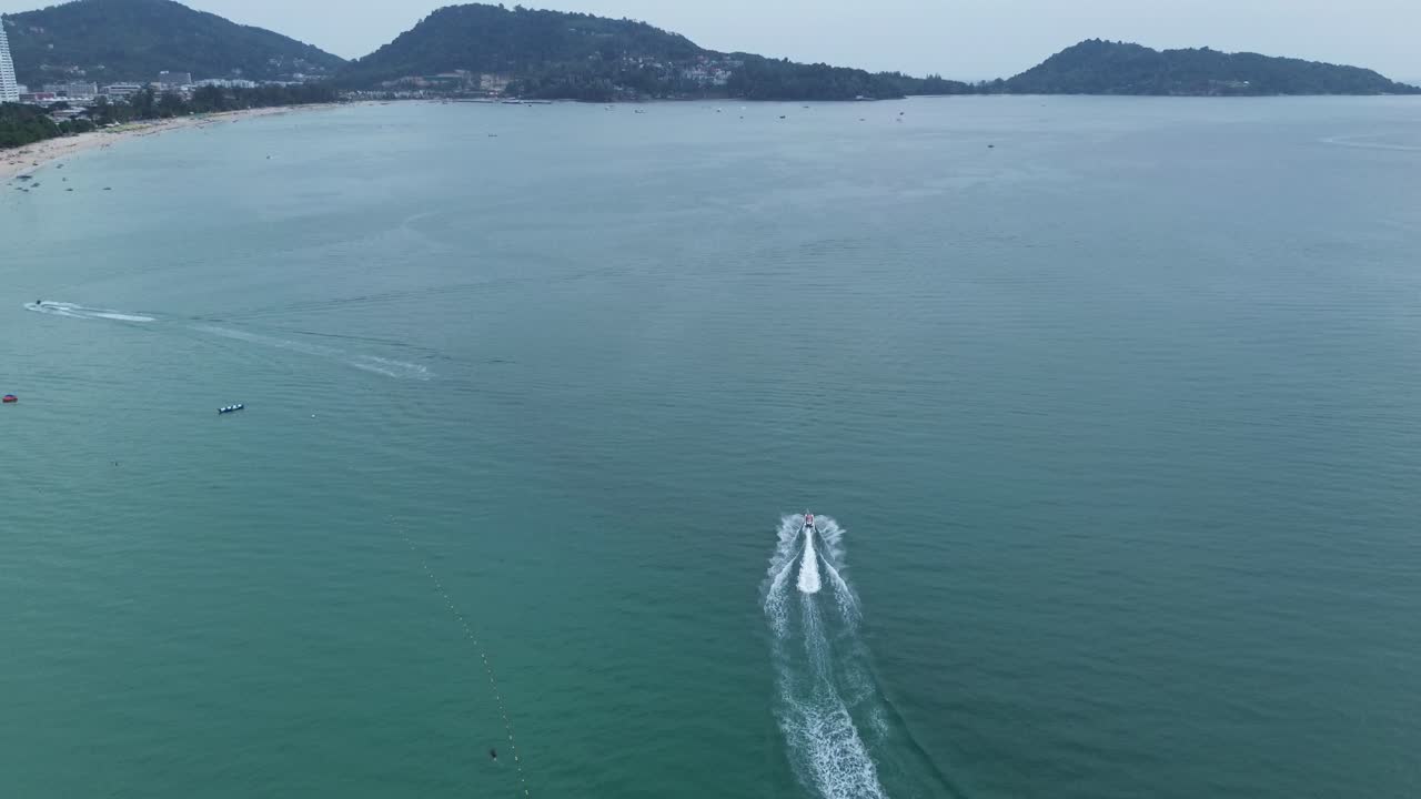 Drone shot with rising angle following a motorboat leaving trail on calm turquoise waters in Phuket