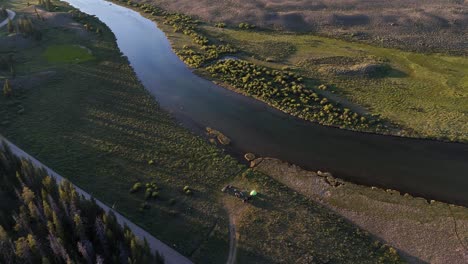 Aerial footage shows calm river curving through open grassland and forest in West Virginia during sunset, highlighting natural textures, tree shadows, clear water, and peaceful terrain below