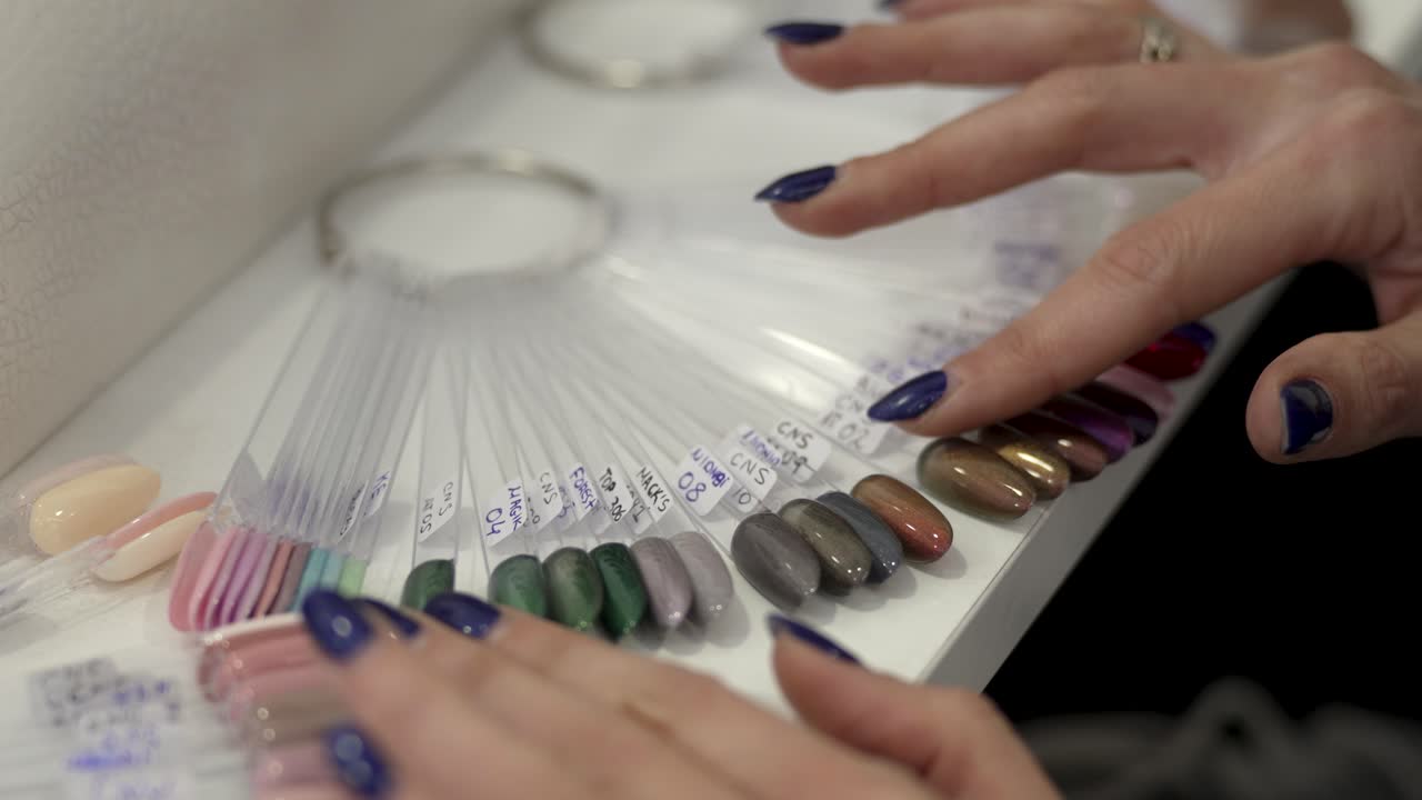 A woman's hand with dark blue manicure leaf through and pick over sample of nail polish colors, close-up