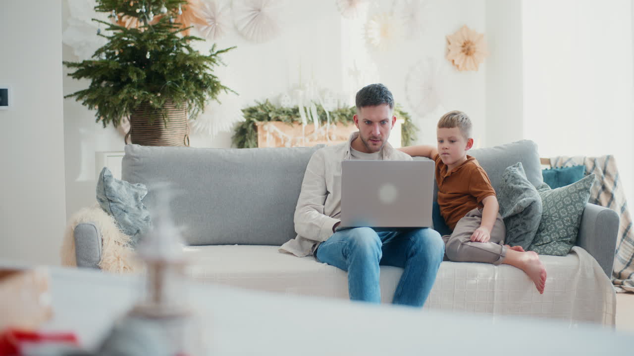 Young Boy Accompanies Dad While Working Remotely on Laptop During Christmas