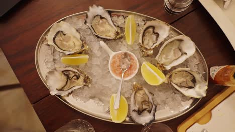 top down view of oysters plate with lemon slices placed on ice, wooden table