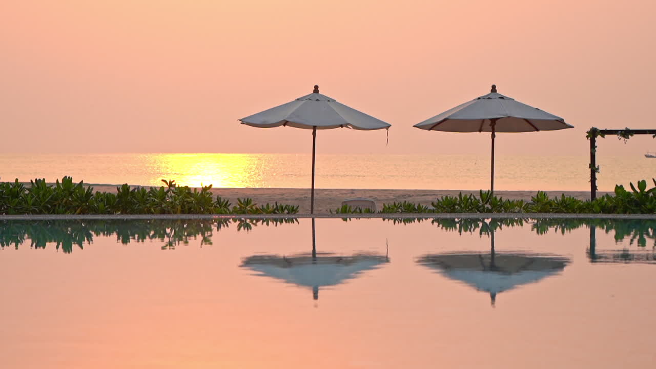 열대 석양의 주황색 선이 바다와 리조트 수영장에 반사됩니다.