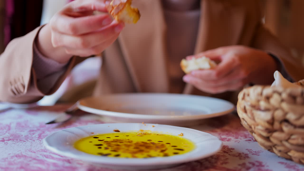 Close up of a woman dipping bread in olive oil with balsamic glaze drops and eating it at a restaurant