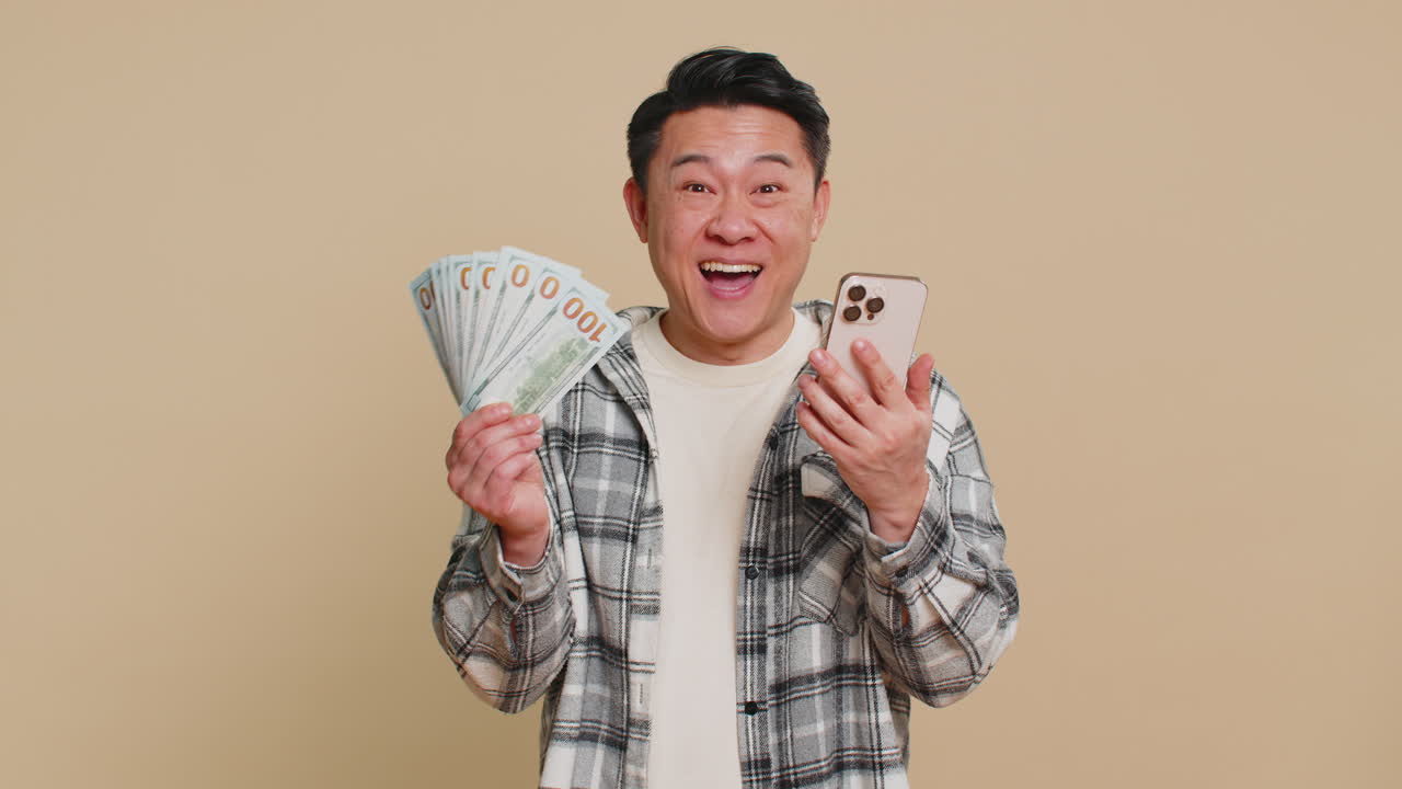 Happy asian man use smartphone rejoicing game win receiving money dollar cash celebrating success