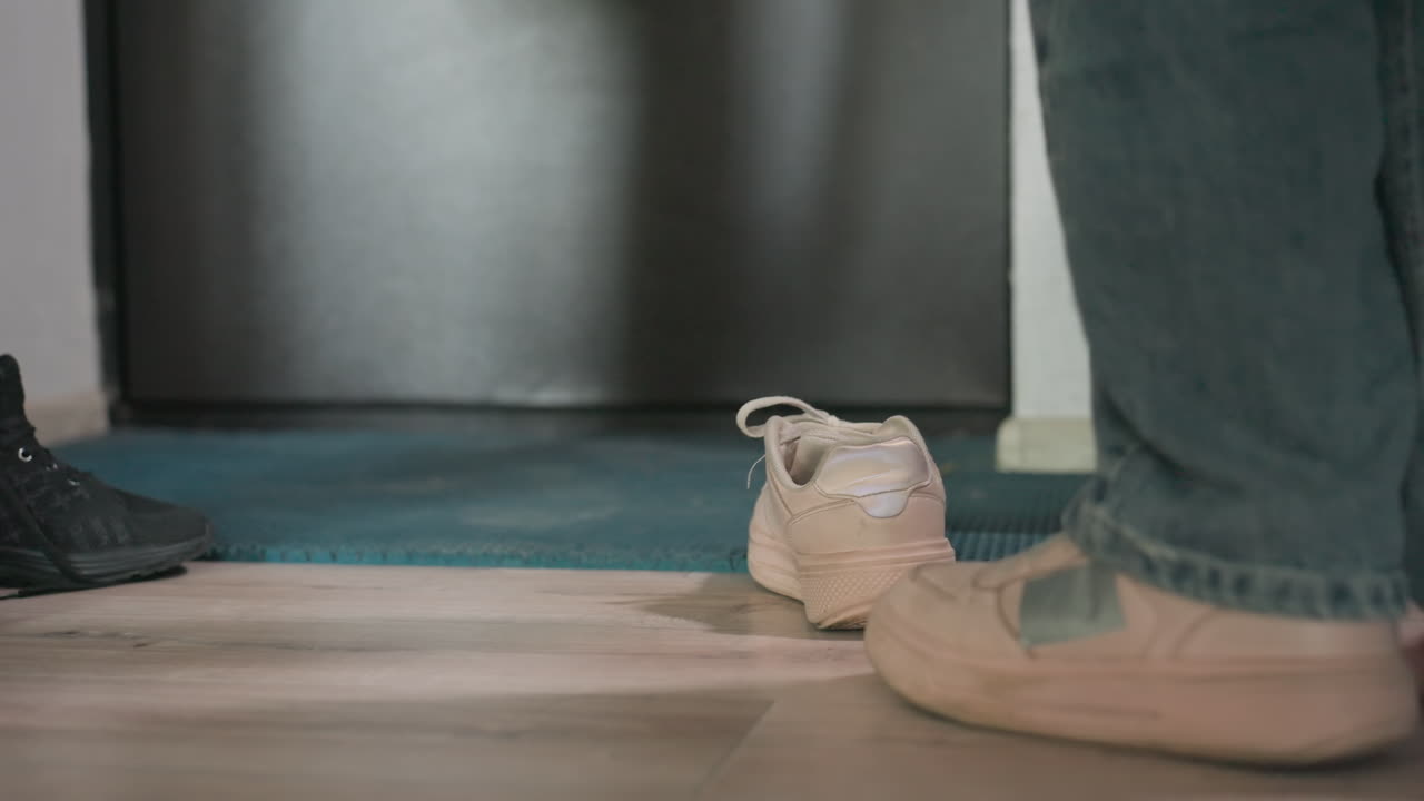 Parent Removes Shoes As Child Stands Barefoot Nearby, Warm Domestic Setting With Natural Light And Cozy Ambiance, Loving Family Moment With Shoes At Door And Relaxed Home Environment