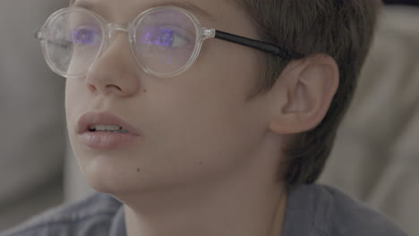 young boy wearing glasses gazes up at the tv screen