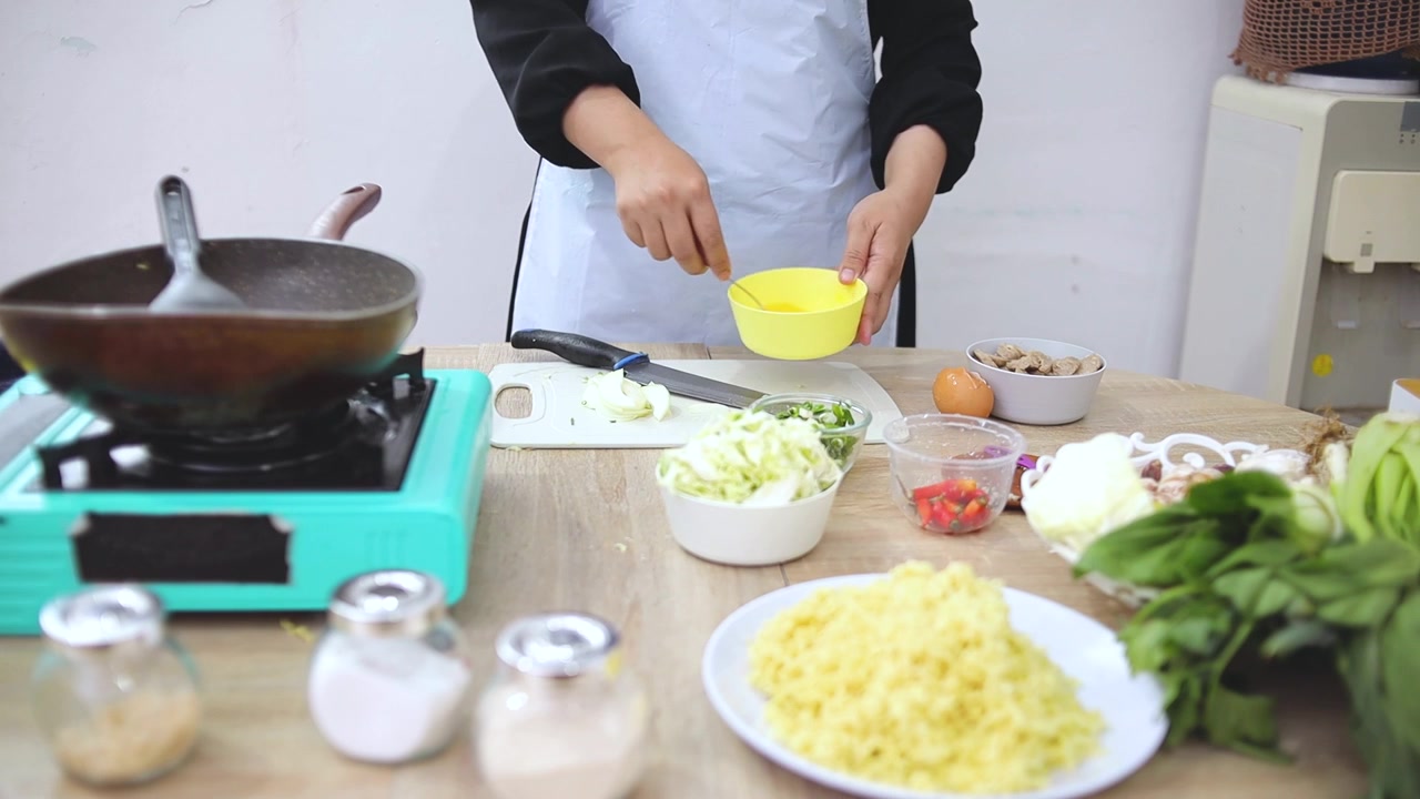 Koki memecahkan telur ke dalam mangkuk kuning kecil saat menyiapkan makanan di dapur