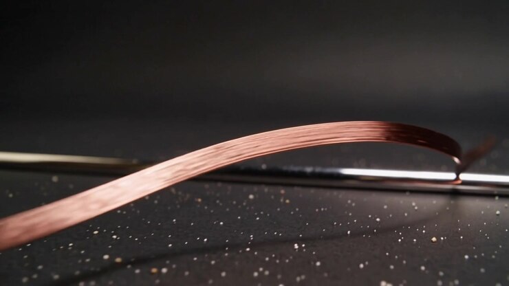Arcing copper ribbon sweeping rightward across studio tabletop, gliding over chrome rod