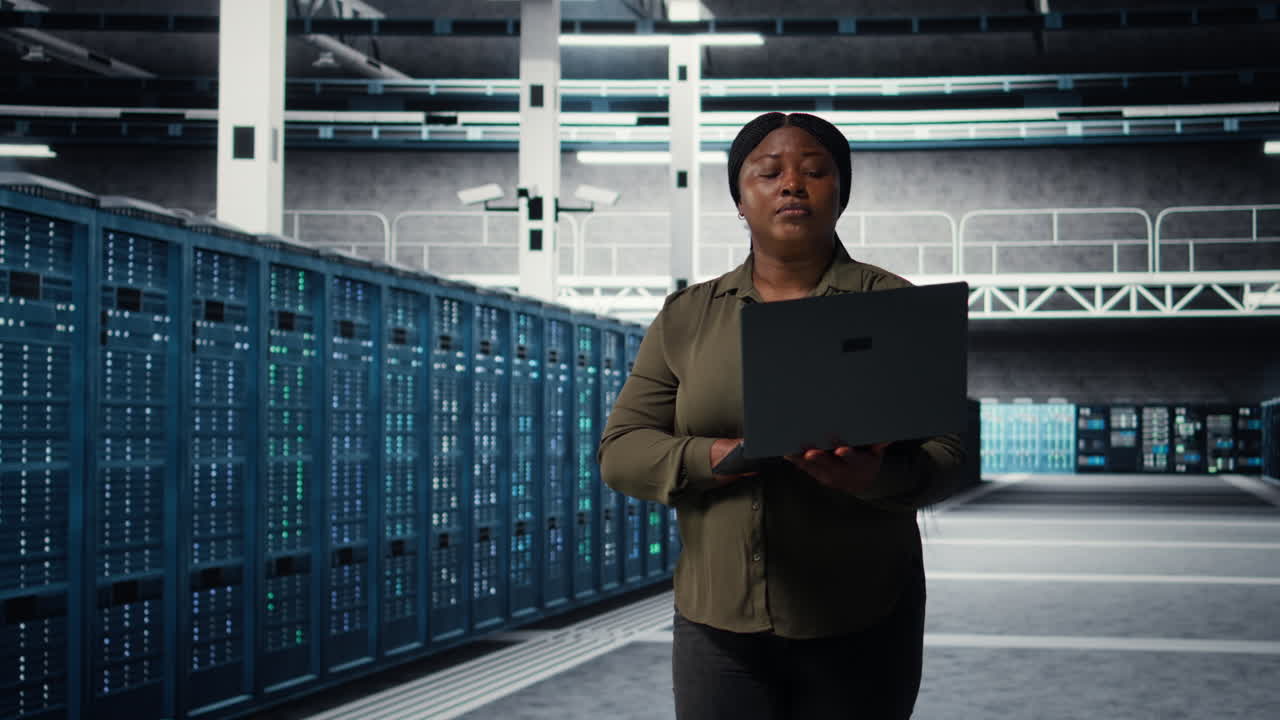 Smilende ingeniør går i datacenter med bærbar computer og tjekker hardware