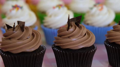 a table with many different flavoured muffins, all with various icing and toppings.