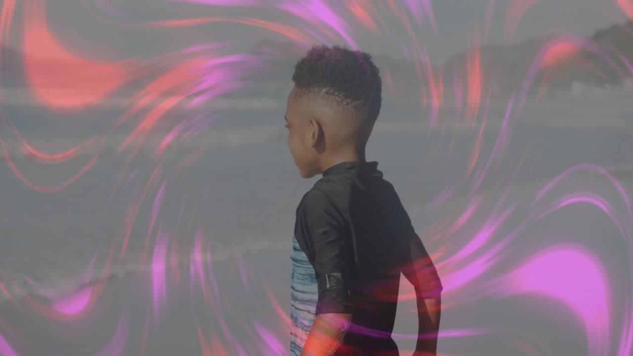 Boy standing facing ocean on beach with swirling colored light trails overlaying technology concept