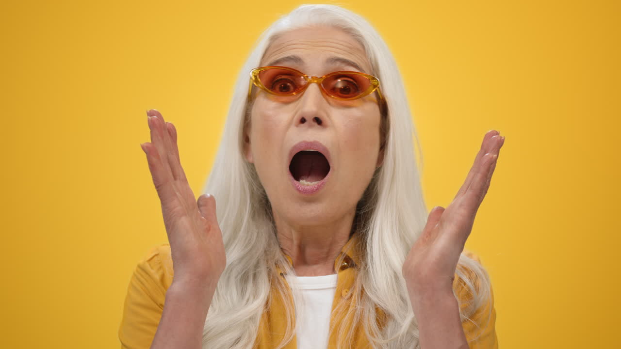 놀란 고령 여성이 안에서 입을 열고, 노인이 스튜디오에서 손을 들고 있습니다.