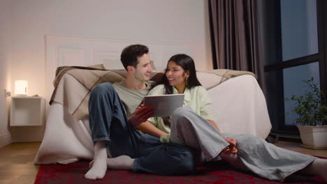 pareja viendo una escena de película inesperada en una tableta mientras se sienta en el suelo en casa