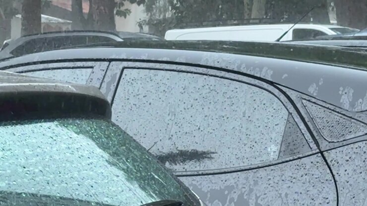 Pioggia torrenziale si abbatte sui veicoli parcheggiati durante un intenso temporale urbano, con l'acqua che scorre sui finestrini e sulla superficie stradale, illustrando condizioni meteorologiche avverse e difficoltà alla guida
