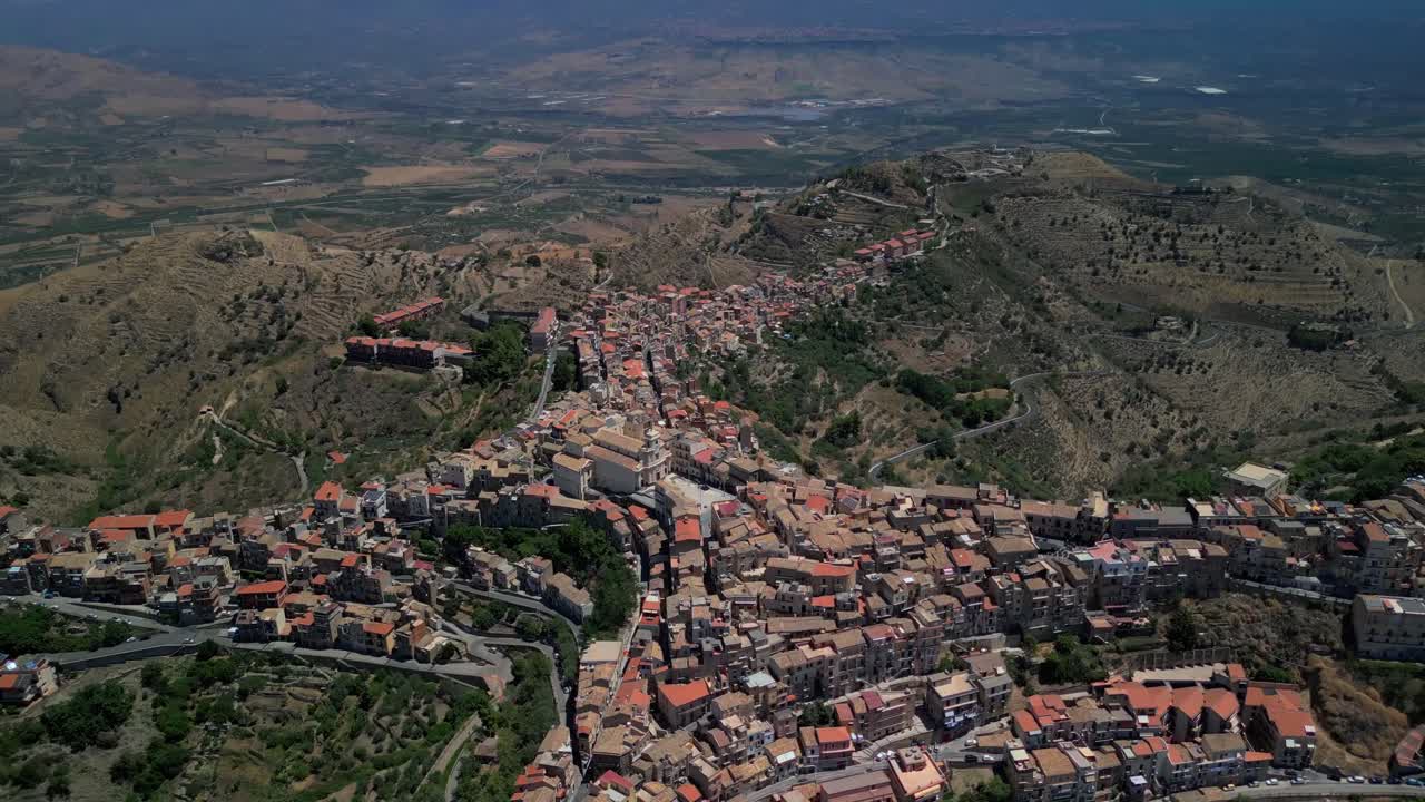 Ampia ripresa cinematografica aerea di Centuripe con il Monte Etna che si staglia contro il cielo serale. Vista aerea che evidenzia la vastità dei paesaggi interni della Sicilia intorno a Centuripe
