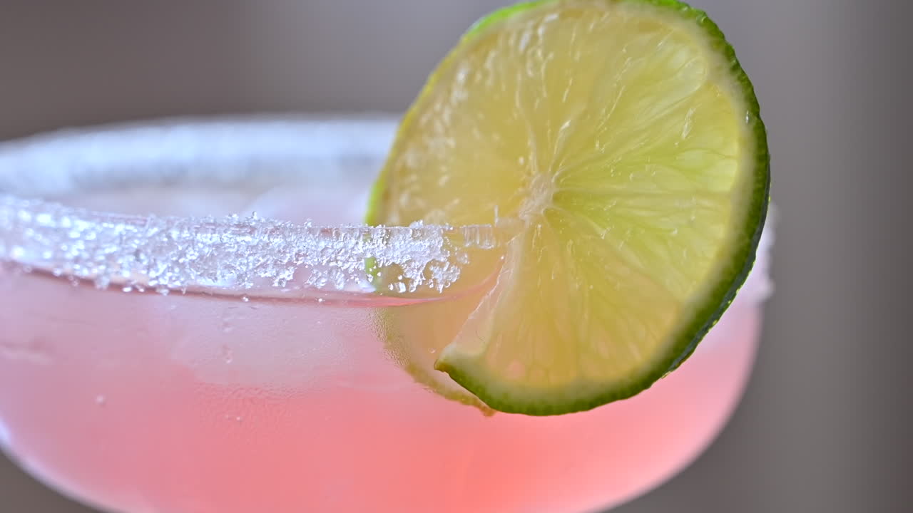 Primer plano de un cóctel rosa claro con hielo y rodajas de lima