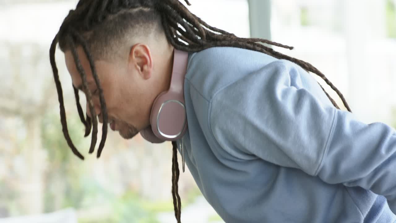 Man starting neck stretching bending forward lifting arms by glass wall with headphones, refreshing