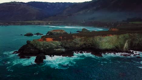 static aerial wide view of waves crashing on rocky ocean cliffs at sand dollar beach in big sur california at twilight