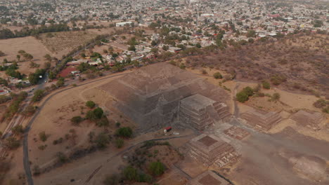 Slide-and-pan-aerial-footage-of-Pyramid-of-the-Moon.-Houses-in-urban-neighbourhood-in-background.Ancient-site-with-architecturally-significant-Mesoamerican-pyramids,-Teotihuacan,-Mexico