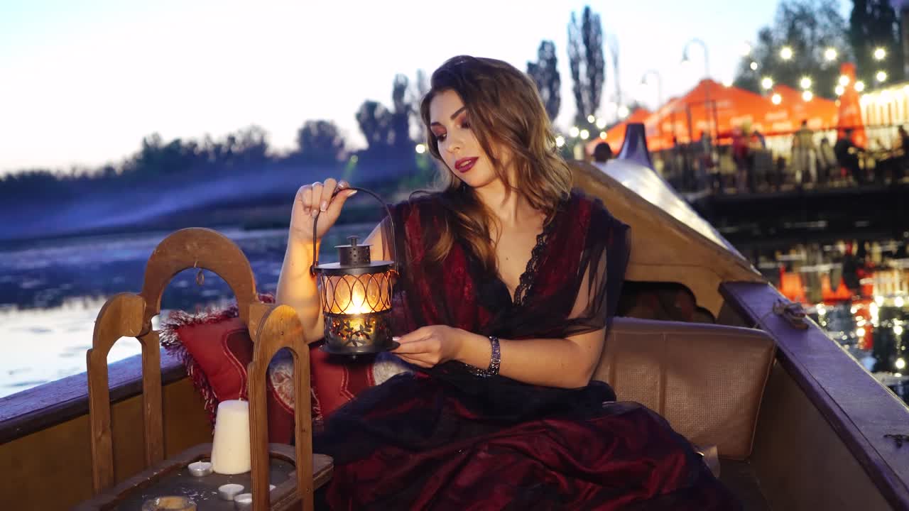 Woman traveling by boat at sunset with a night lamp in hands. Gondola floating along the river