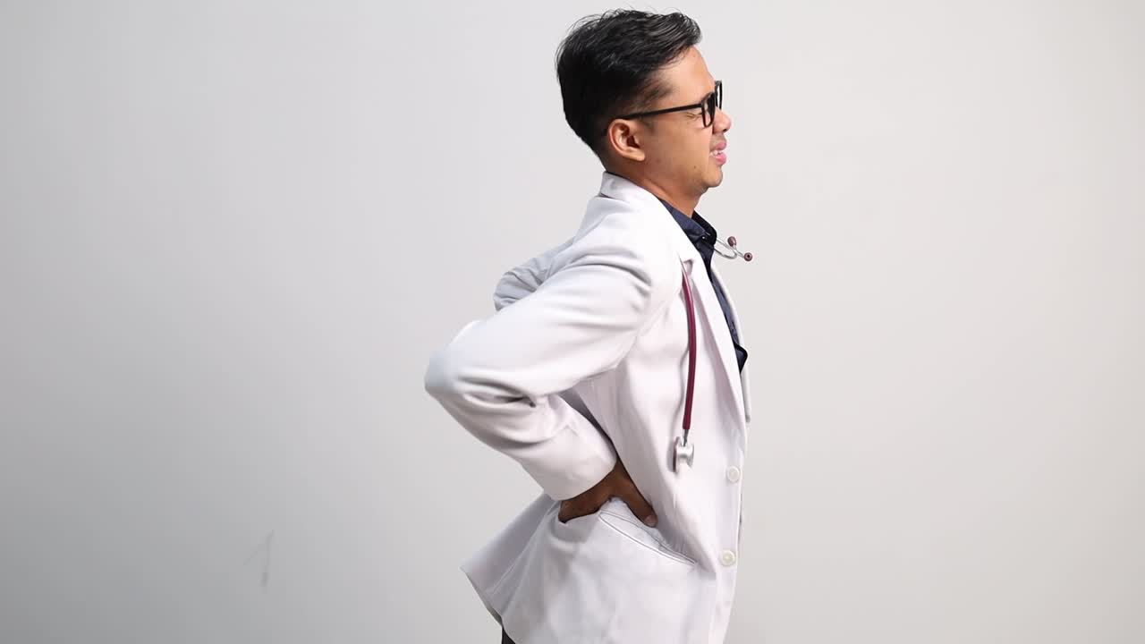 Young Asian doctor man experiencing lower back pain and discomfort with soothing massage for relief
