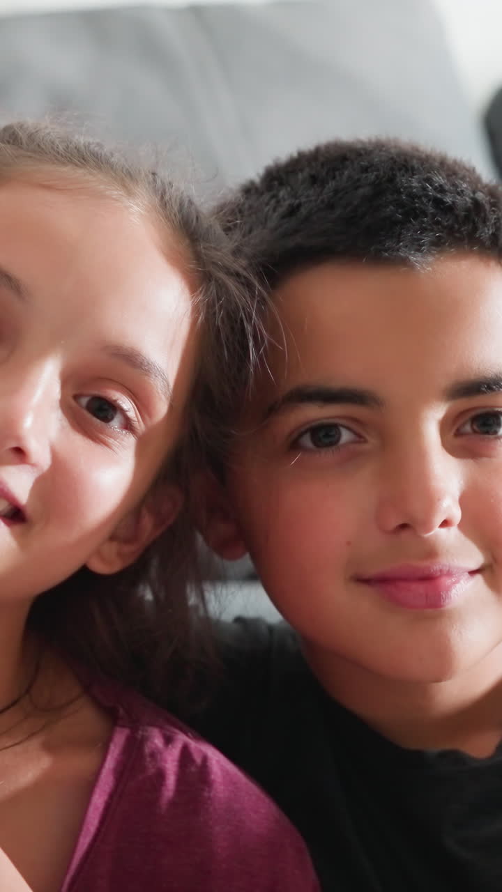 Precioso momento de hermanos sentados muy juntos en el sofá, sonriendo cálidamente con los brazos entrelazados, mostrando un fuerte vínculo y afecto en un acogedor ambiente hogareño con luz natural