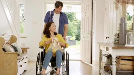 mature asian man pushing wife in wheelchair in hallway at home returning from shopping trip holding reusable bag - shot in slow motion