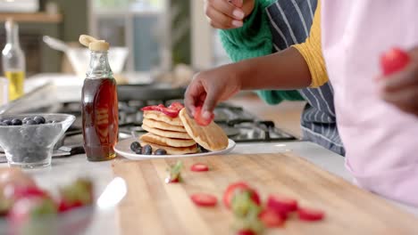 hands of african american mother and daughter decorating pancakes with fruits, slow motion