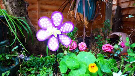 colourful rotating childlike butterfly windmill blowing in breeze between assortment of blossoming flowers and plants