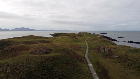 aerial push in view ynys llanddwyn island anglesey coastal walking trail with snowdonia mountains across the irish sea