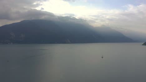 Dolly-in-aerial-shot-of-Lake-Garda-with-the-morning-sun-breaking-through-the-clouds-and-spilling-light-over-the-majestic-mountains