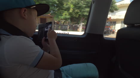 child taking mobile photos of town during car ride