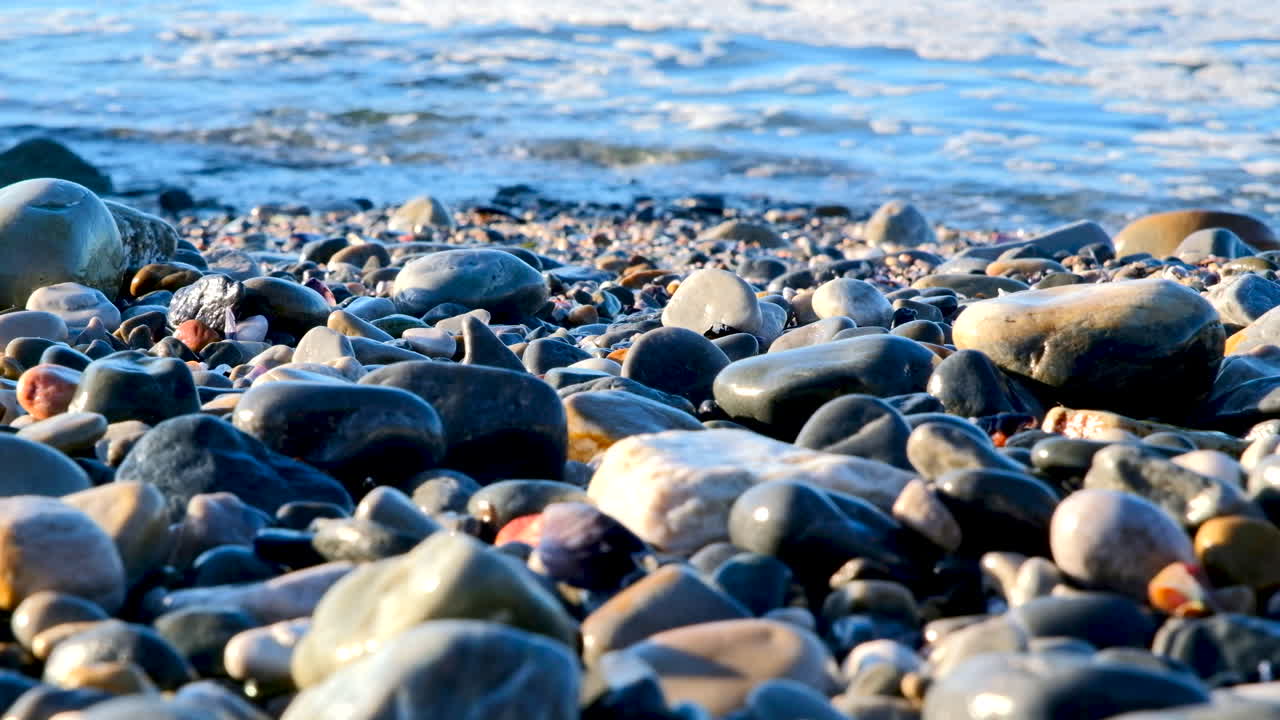 Relaxing sunrise scene as waves lap onto coastline with smooth pebbles and rocks