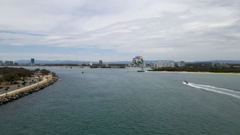 Vista-Aérea-De-Un-Barco-Rápido-Tirando-De-Un-Parasail-Por-El-Aire-Con-El-Horizonte-De-La-Ciudad-En-El-Fondo