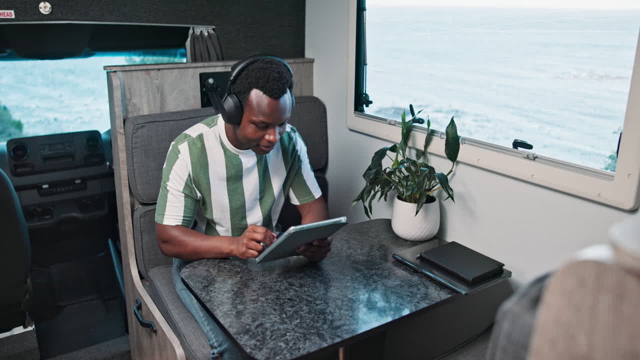 Young Man in Headphones Using Tablet in Camper Van with Ocean View