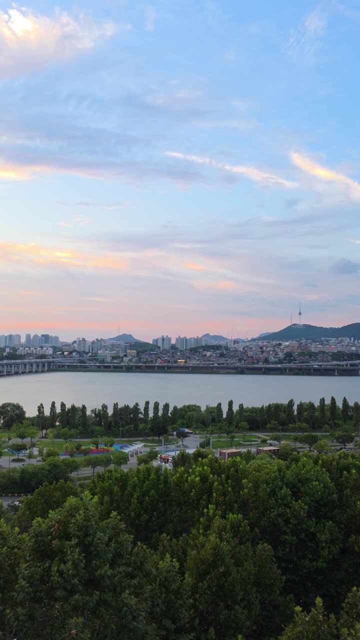 Vertical aerial view of Seoul at sunset with Namsan Tower, Yongsan District, and Hangang River park under colorful evening clouds