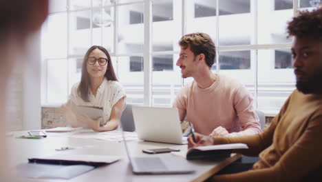 creatives at a table in a meeting room listening to female colleague, selective focus, close up