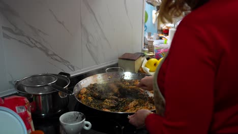 Frau-Gießt-Schwarze-Tintenfischtinte-In-Eine-Paella,-Um-Schwarzen-Reis-Zu-Kochen,-4k