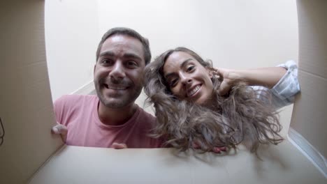 joven pareja feliz abriendo caja de cartón después de la reubicación, mirando dentro y sonriendo
