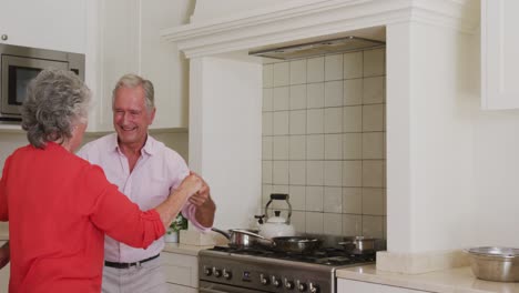 happy caucasian senior couple having fun smiling and dancing in kitchen