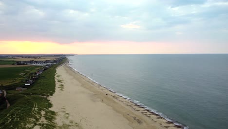 Weite-Landschaftsantenne-über-Einem-Wunderschönen-Sandstrand-Bei-Sonnenuntergang-Mit-Ruhigem-Meer