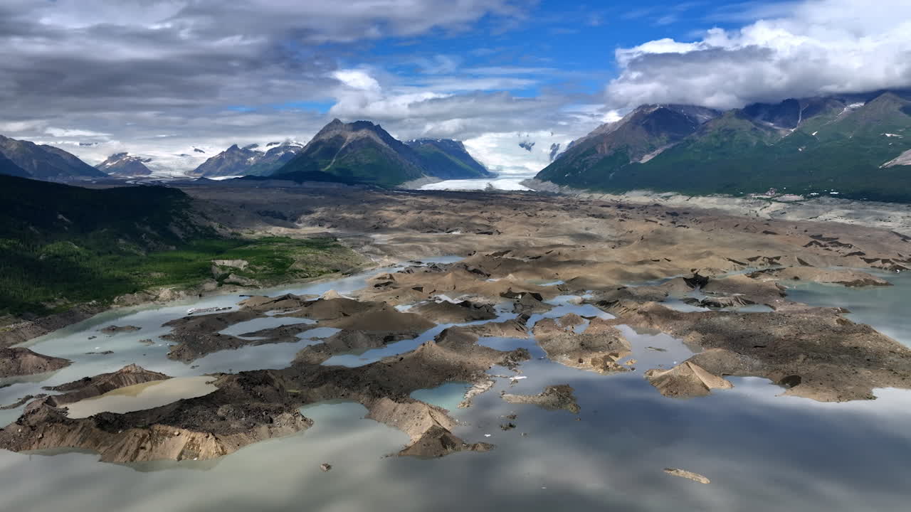 Melting ice in the valley among the mountains. Fluffy clouds are in the sky over the rocks. Alaska, USA