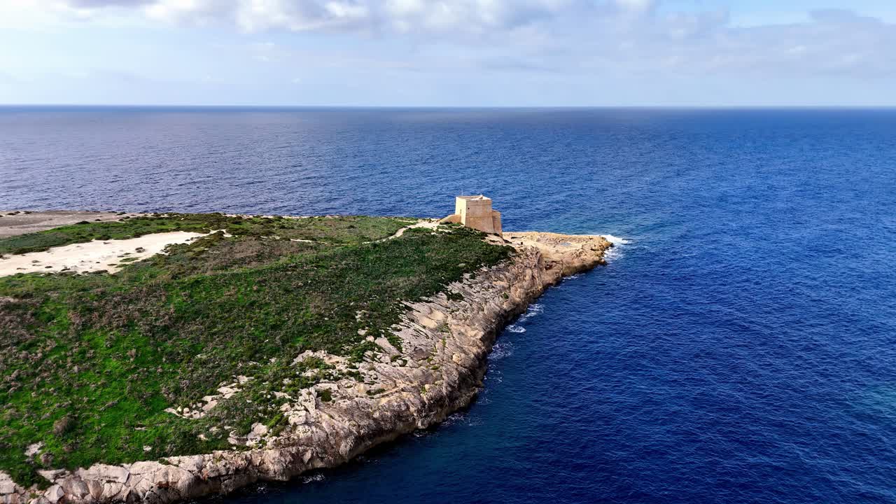 Prospettiva aerea della storica Torre di Qawra, sentinella sulle spettacolari scogliere calcaree e le acque blu intenso del Mediterraneo in una giornata luminosa e soleggiata sull'isola di Gozo, Malta