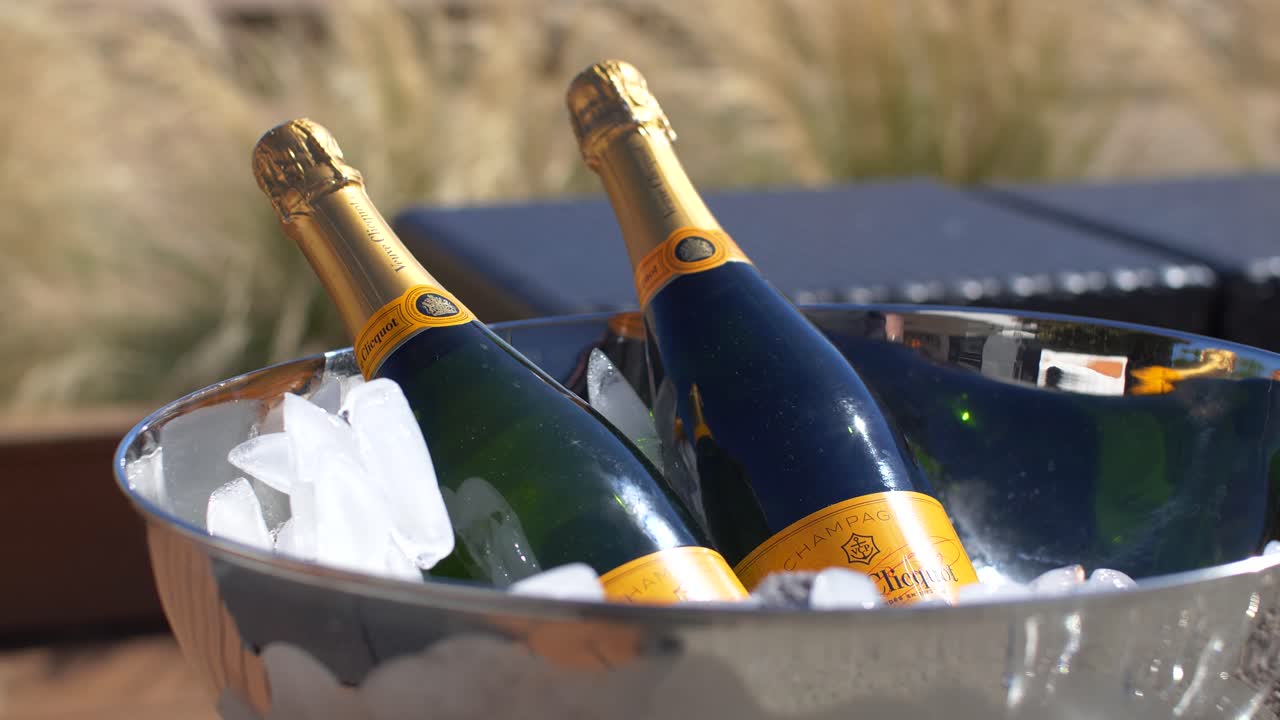 dos botellas de champán veuve clicquot en tazón de plata y hielo frente a la hierba bajo el sol