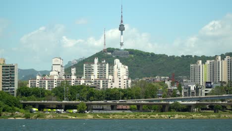 Patrol-vessel-on-Hanriver,-Namsan-Seoul-N-tower-and-traffic-on-highway-in-Yongsan-district,-South-Korea