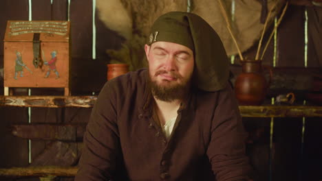 a man in medieval clothing sits in a rustic cabin