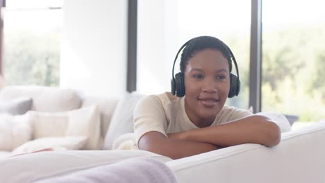 Happy-african-american-woman-sitting-on-sofa-using-headphones-and-listening-to-music,-slow-motion